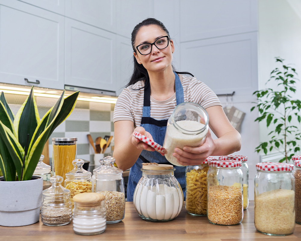 Uma mulher na cozinha mostra frascos para guardar alimentos secos.