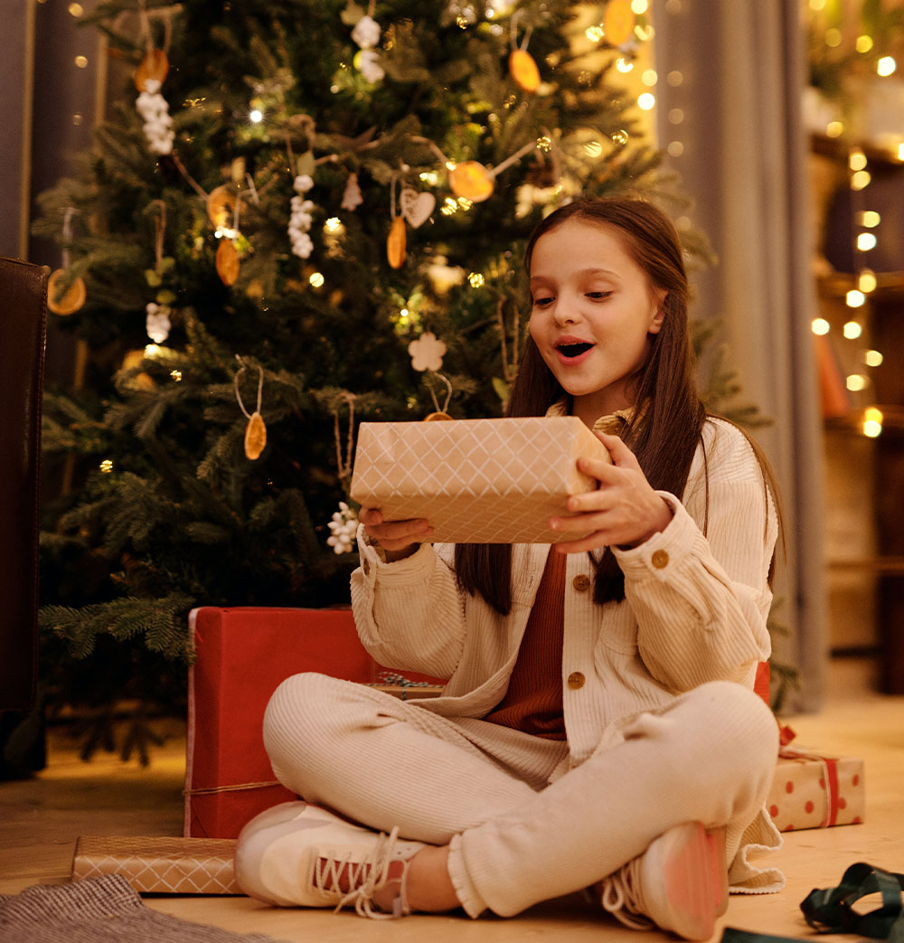 Uma rapariga desfruta de um presente debaixo da árvore de Natal.