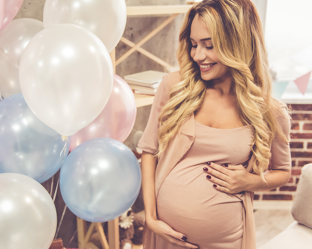 Mulher grávida a olhar com um sorriso para os balões coloridos durante a babyshower