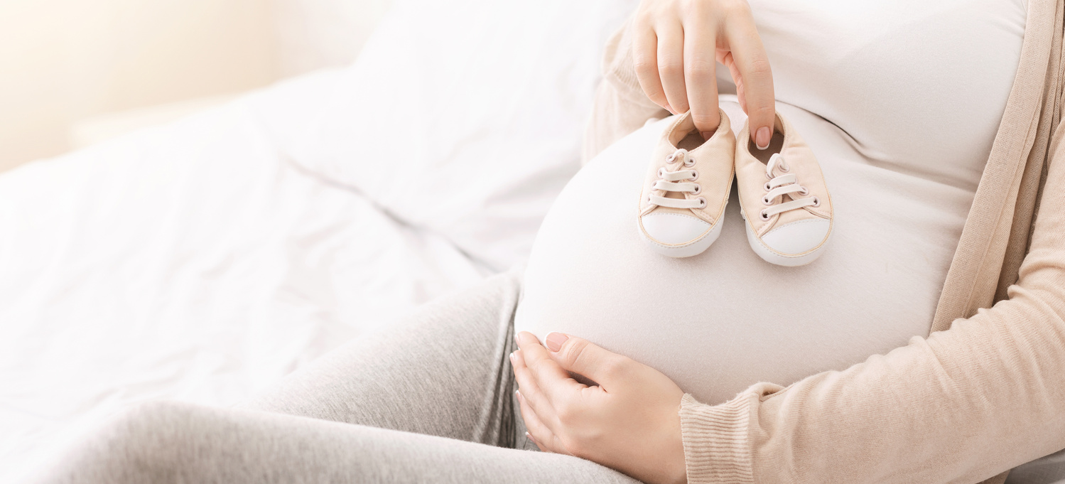 Mulher grávida a segurar sapatos de bebé na barriga