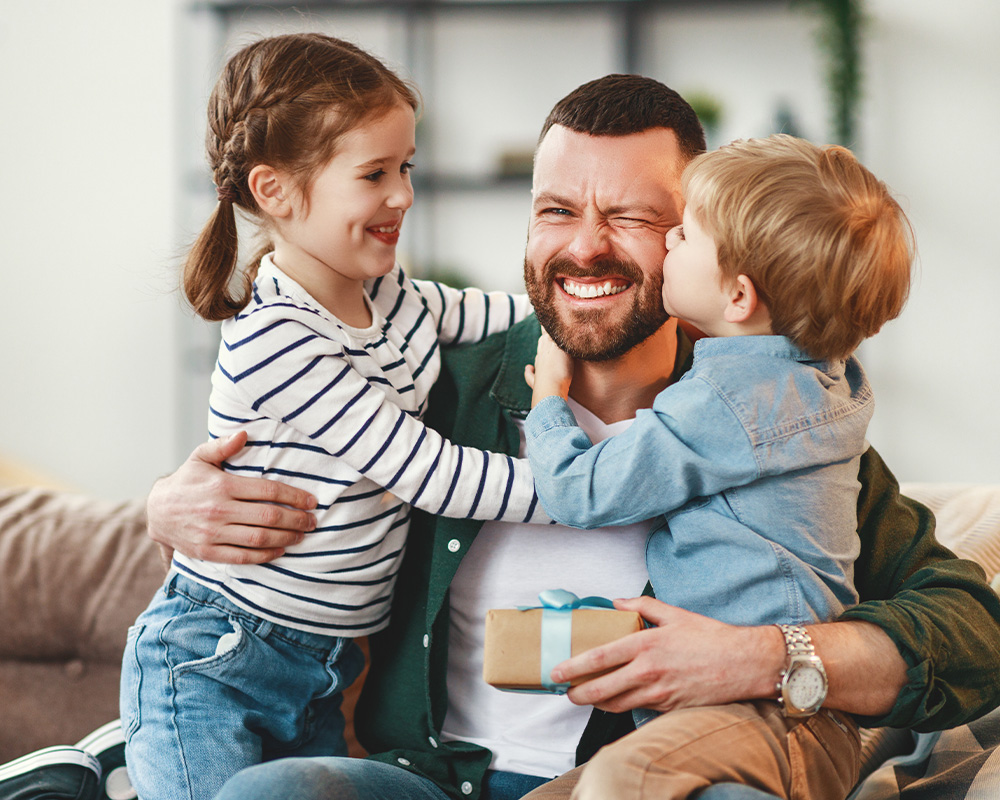 Um pai abraça dois filhos e segura uma prenda nas mãos