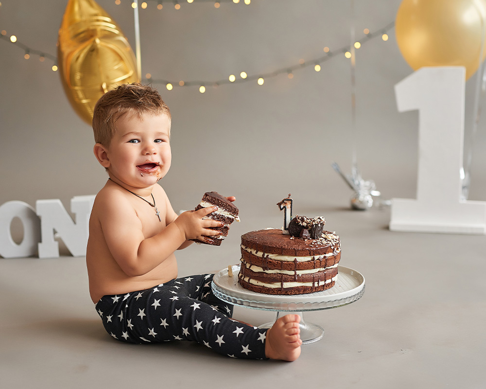 Um menino de um ano segura um pedaço de bolo de chocolate nas mãos para celebrar o seu aniversário