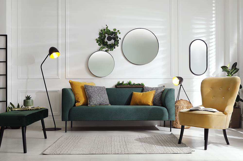 Sala de estar moderna em tons claros com um sofá verde, almofadas amarelas e espelhos redondos na parede.