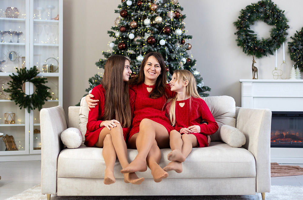 A mãe e as suas filhas, com vestidos vermelhos, passam juntas a época natalícia junto à árvore de Natal.