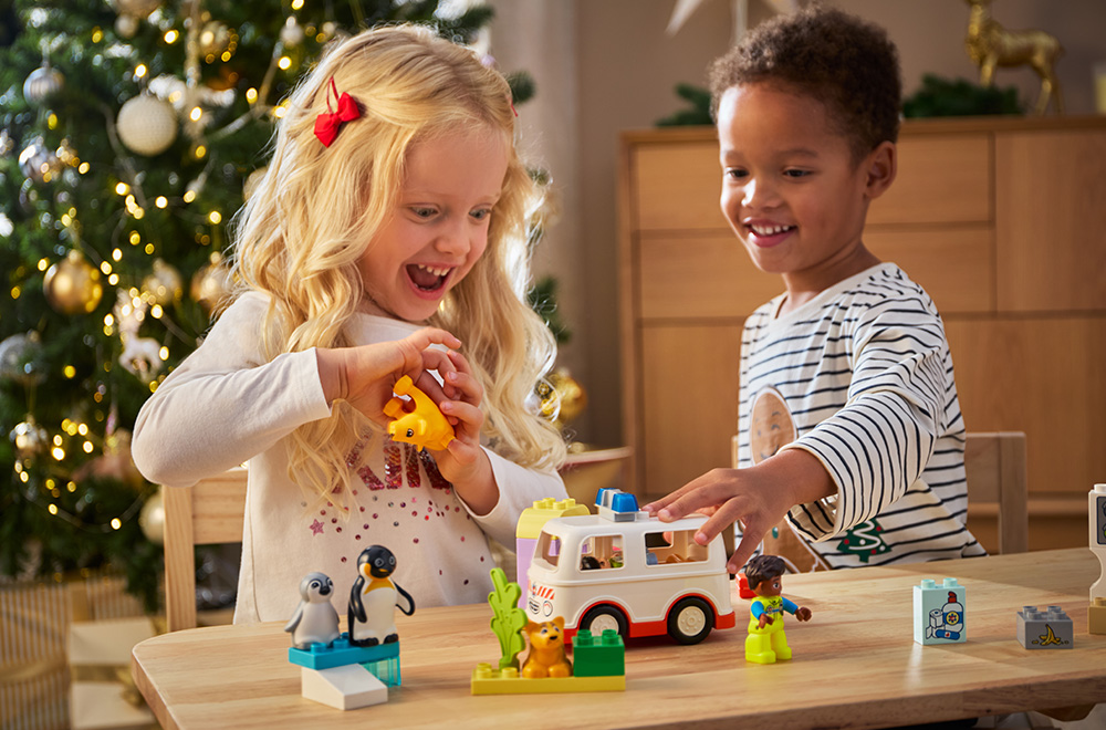 Duas crianças brincando com blocos de LEGO sob a árvore de Natal.