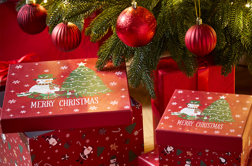 Caixas de presentes com motivos de Natal ao lado da árvore de Natal.