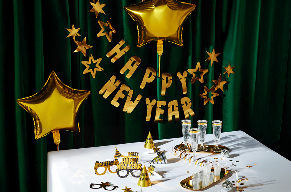 Mesa decorada para o Ano Novo, com balões, copos e enfeites dourados.