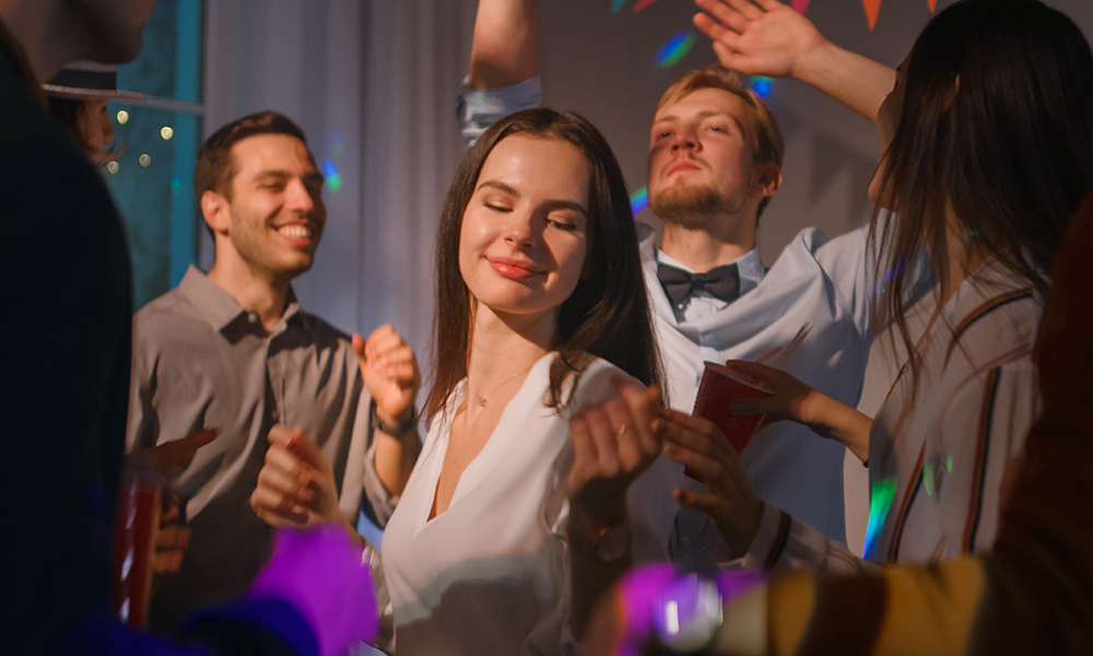 Um grupo de pessoas dançando em uma festa, entre as quais há uma mulher se divertindo com a música.