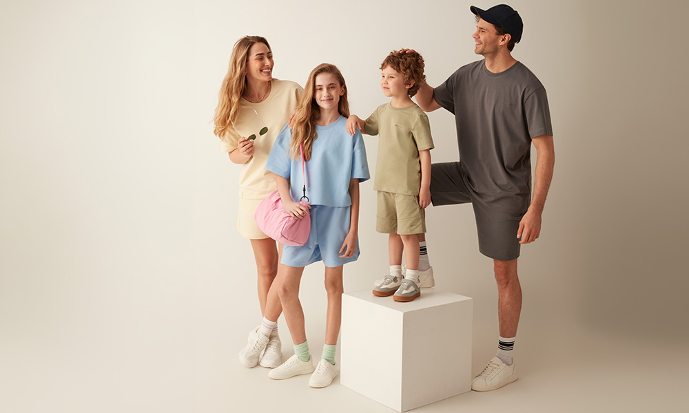 Uma família com roupa em tons pastel posa junta sobre um fundo claro.